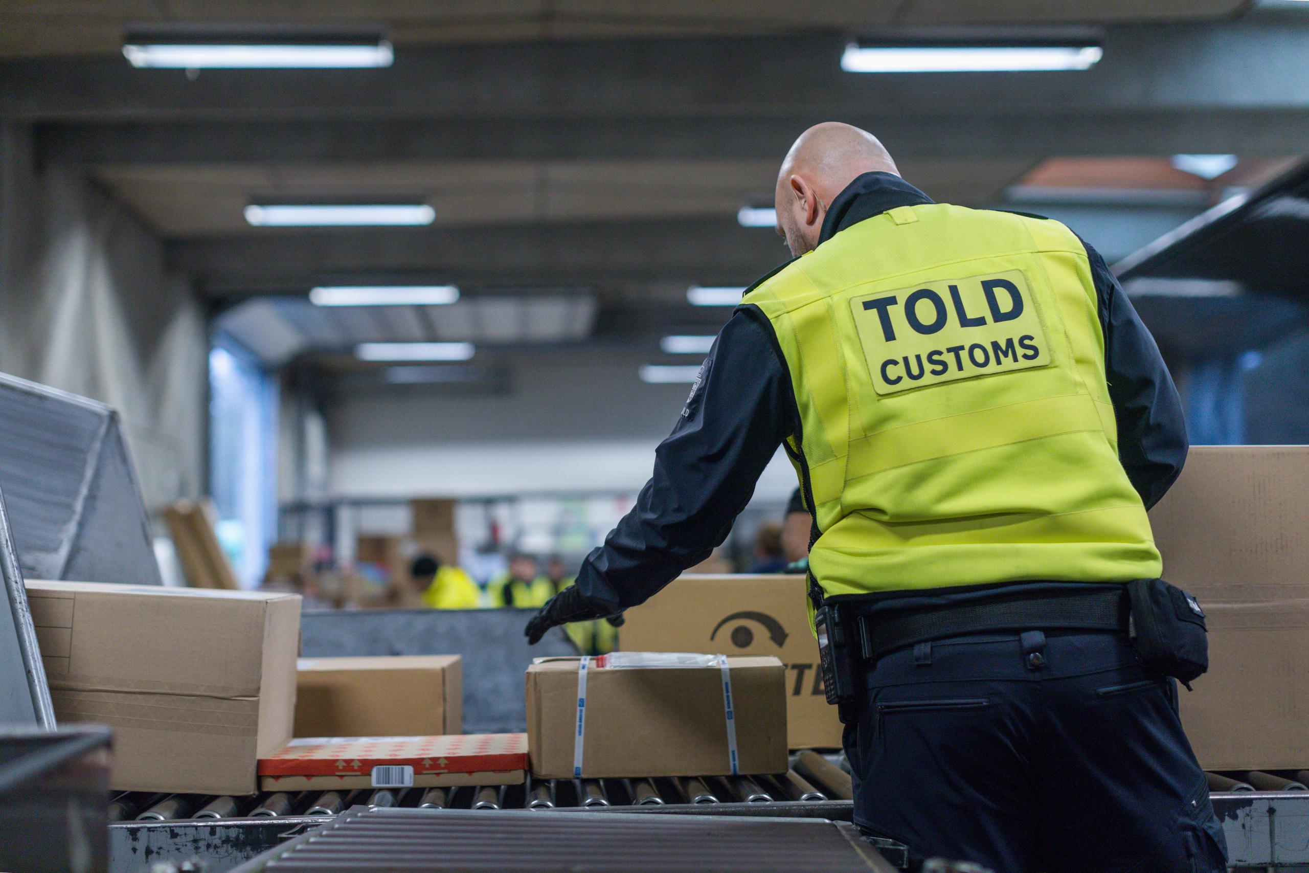 Tolder kontrollerer pakker på et pakkebånd